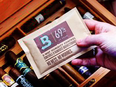 Male hand holding a 69% RH Boveda and placing it in a hood humidor with cigars
