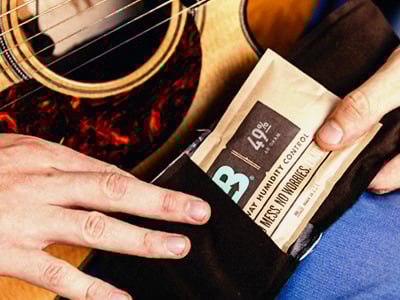 A male hand placing a B49 Boveda into a fabric holder over an acoustic guitar